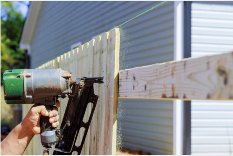 Contractor installing a wood fence with a nail gun
